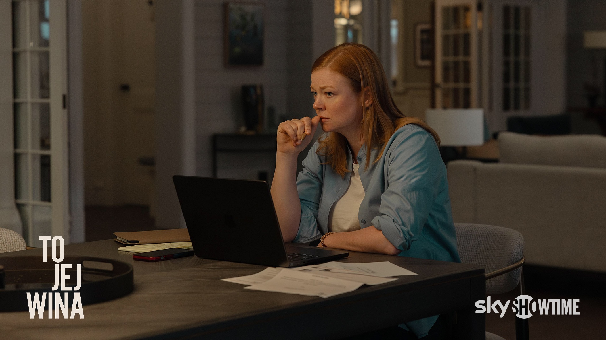 Kadr z serialu To jej wina przedstawiający zamyśloną główną bohaterkę siedzącą przy stole w nowoczesnym salonie.