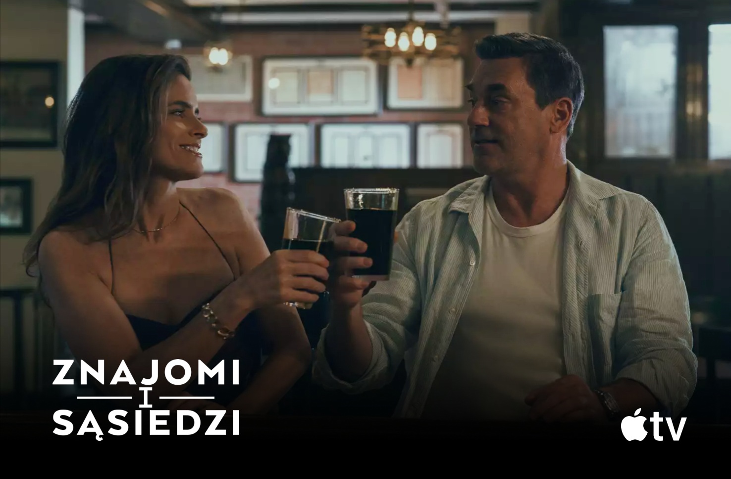 Mel i Jon siedzący przy stoliku i wznoszący toast szklankami z napojem