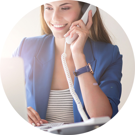 Uśmiechnięta kobieta rozmawia przez telefon stacjonarny, używając laptopa