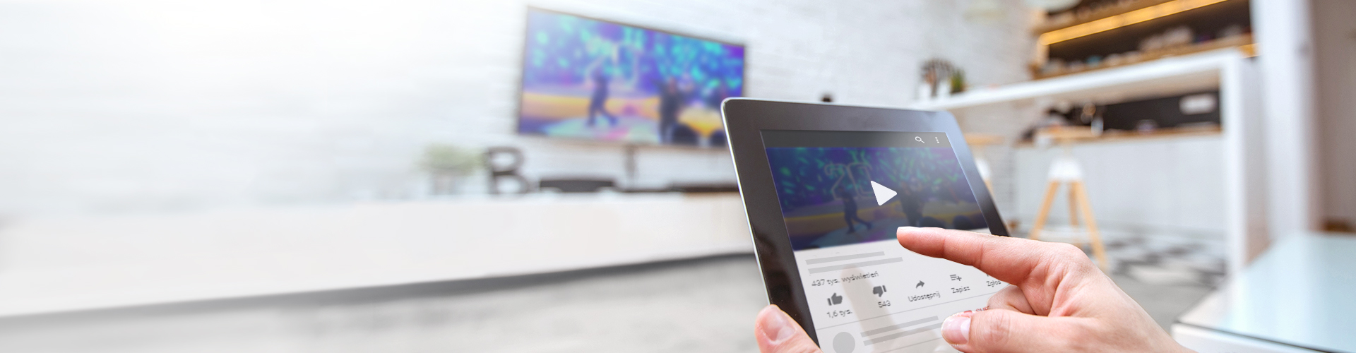 Dłoń trzymająca tablet na tle telewizora